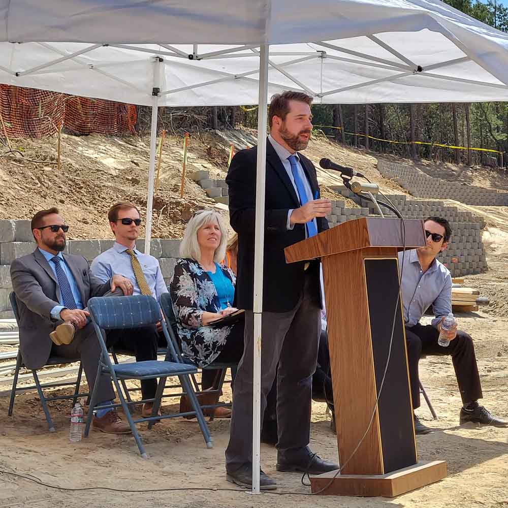 Ryan Campbell speaking at outdoor groundbreaking ceremony. Fellow Tuolumne County Supervisors are sitting behind him. 